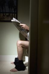 Mature man reading newspaper on toilet, side view, low section